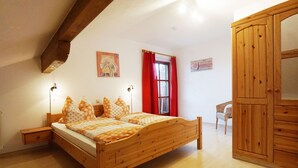 A bedroom with a wooden bed, bedside lamps, a chair, and a wardrobe. - Ferienwohnung III im 2. Stock mit Balkon, Wohnküche, Schlafzimmer, Dusche/wc, Balkon (Chieming)