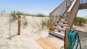 Eine Holztreppe führt zu einem Sandstrand mit Liegestuhl und einem grünen Gartenschlauch.
