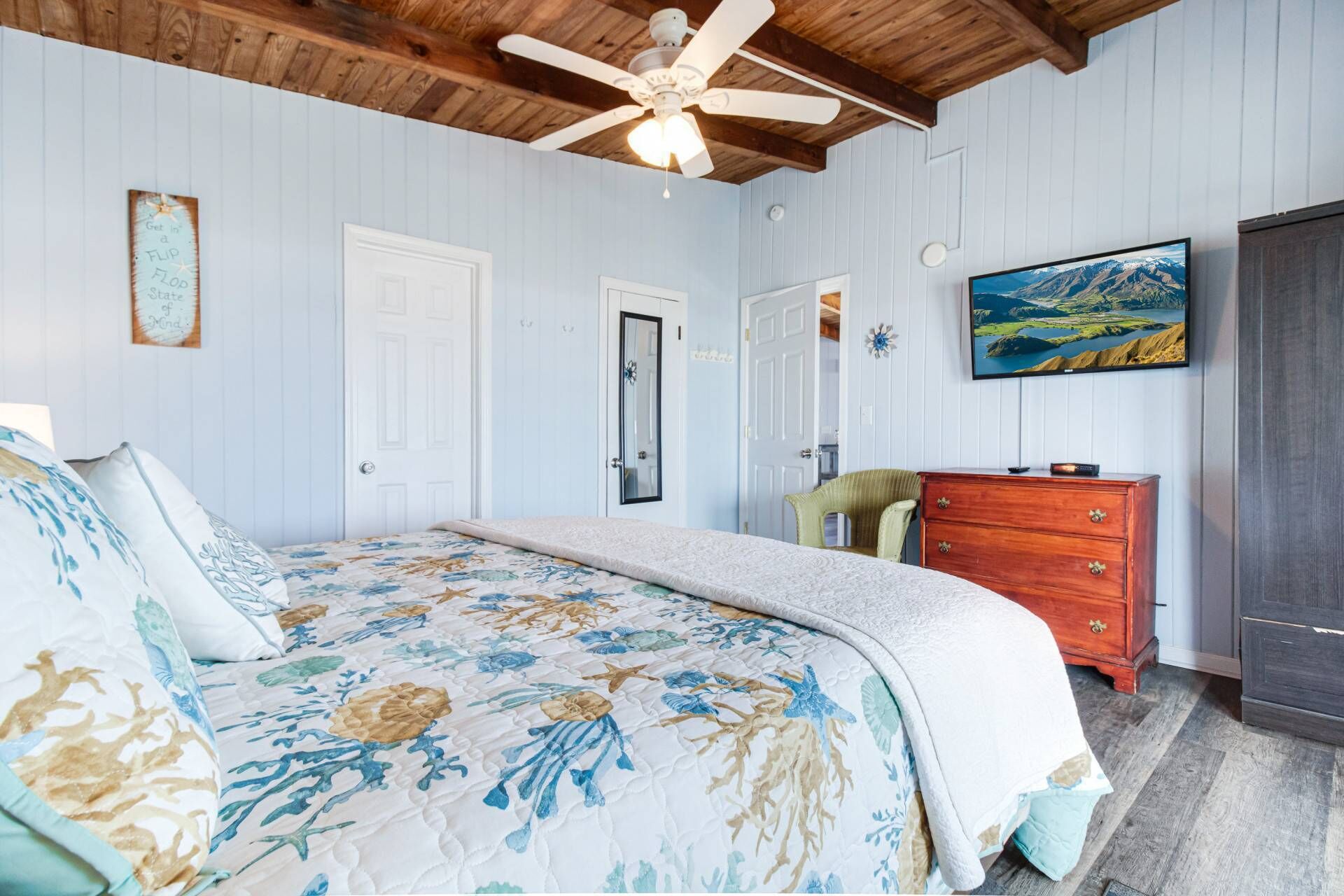 A bedroom with a bed, a wooden dresser, a ceiling fan, and a painting on the wall.