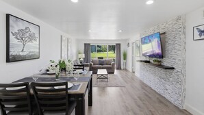 Una sala de estar moderna con comedor, un televisor de pantalla plana en una pared texturizada y vistas a un campo de golf a través de grandes ventanales.