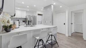 Una cocina moderna con armarios blancos, un refrigerador de acero inoxidable, horno empotrado y una isla grande con taburetes de bar.