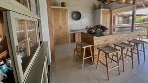 A kitchen with a wooden island, stools, and a view of the outdoors. - Villa Biarritz (Pecatu)