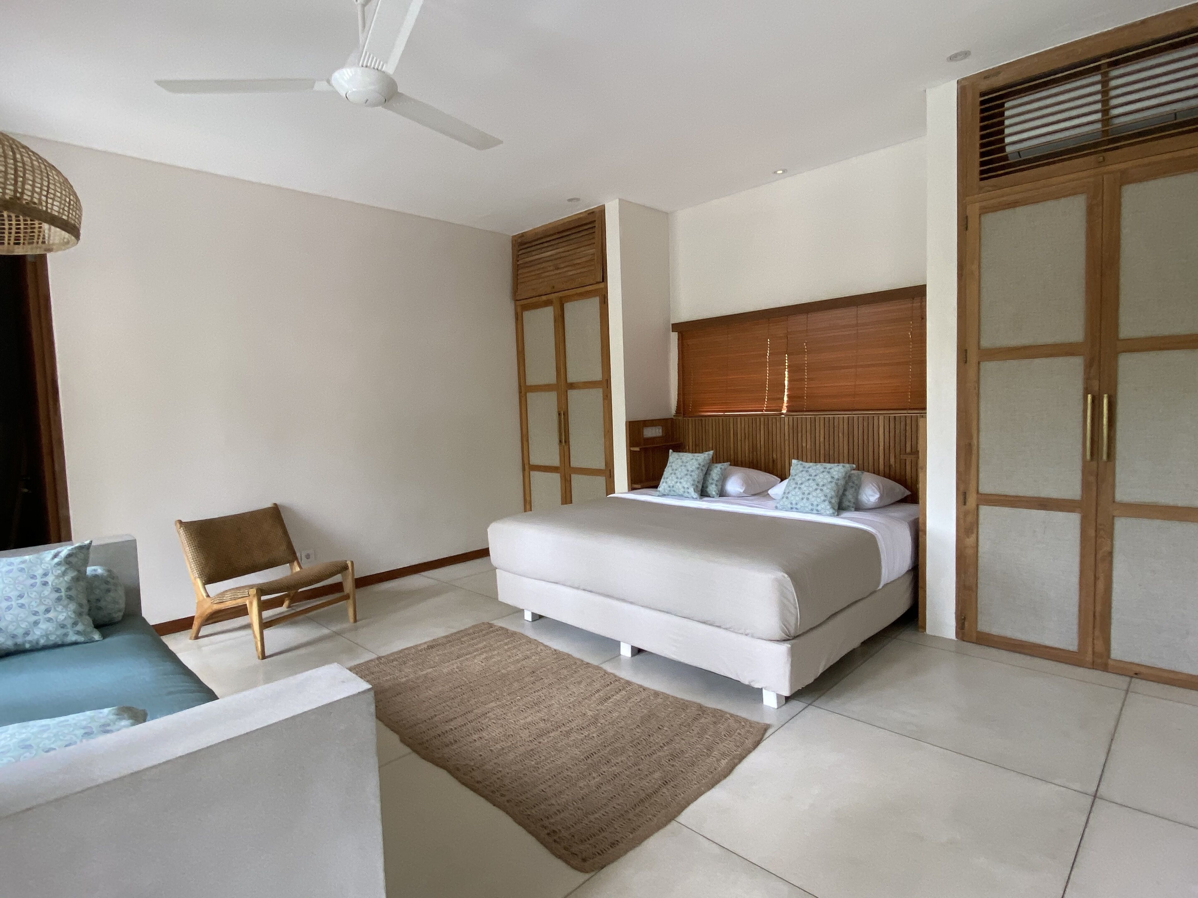 A bedroom with a bed, a chair, a ceiling fan, and a wardrobe.