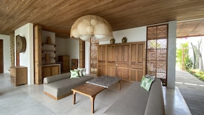 A spacious living area with a wooden ceiling, a large woven light fixture, and a view of a garden through a wooden screen. - Villa Biarritz (Pecatu)