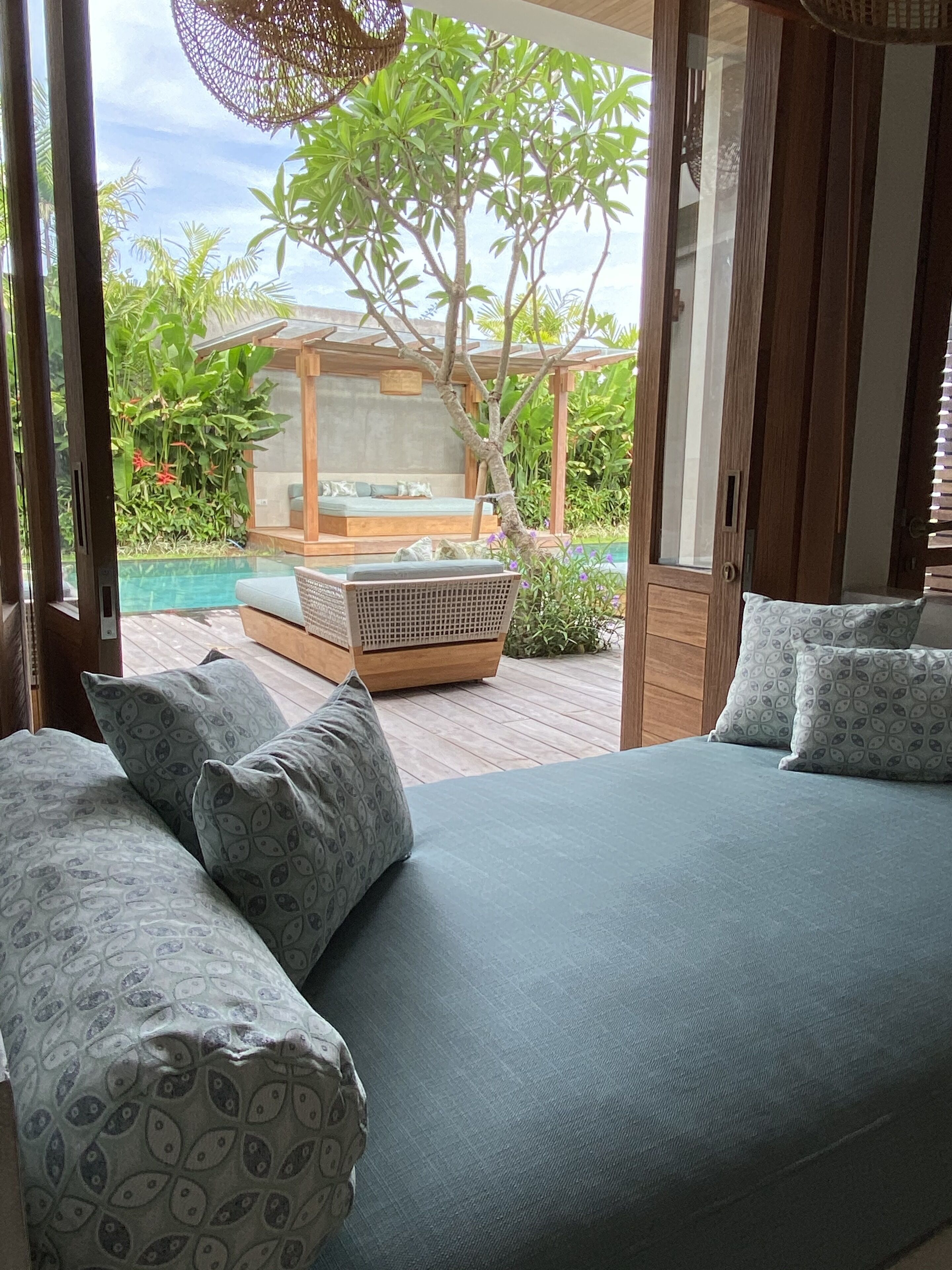 A bedroom with a large bed, a wooden floor, and a view of a pool and garden.