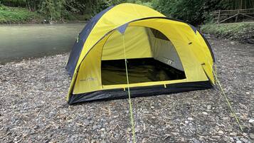 Une tente jaune et noire est installée sur une rive rocheuse, avec une rivière en arrière-plan.