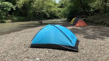 A blue tent on a gravel path with a river and forest in the background.