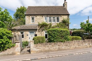 A stone house with a tiled roof, a front door, and a small front garden.