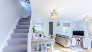 A modern living space with a staircase, a dining area, a sofa, and a TV. - Bright and cosy two bedroom holiday cottage with wood burning stove - Hillcrest Cottage (Avening, near Tetbury)