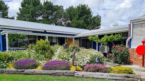 A house with a blue roof, surrounded by a garden with various flowers and a statue. - Cottage Amongst The Vines (Clunes)