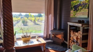 A cozy living room with a large window, a fireplace, and a television. - Cottage Amongst The Vines (Clunes)