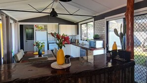 A modern kitchen with a central island, white cabinets, and a dining area with a table and chairs. - Cottage Amongst The Vines (Clunes)