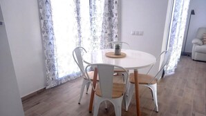 Un comedor con una mesa redonda y cuatro sillas, una pequeña planta en maceta y cortinas con estampado.