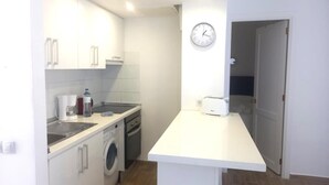 Una cocina compacta con armarios blancos, lavadora, cafetera y tostadora.
