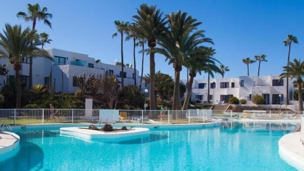 Un área de piscina con varias piscinas, rodeada de palmeras y edificios modernos.