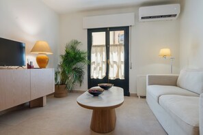 Een moderne woonkamer met een flatscreen televisie, twee lampen, een houten salontafel met een schaal, een bank en een potplant.