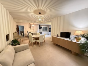 Una sala de estar moderna con comedor, televisor y planta.