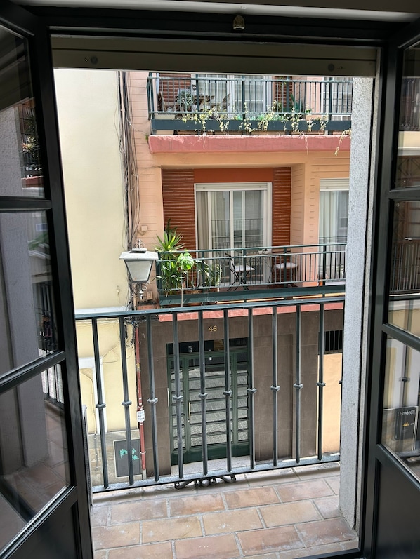 A balcony with a metal railing, potted plants, and a view of a building with a window and a door.
