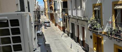 A narrow cobblestone street flanked by buildings with balconies and a clear blue sky.