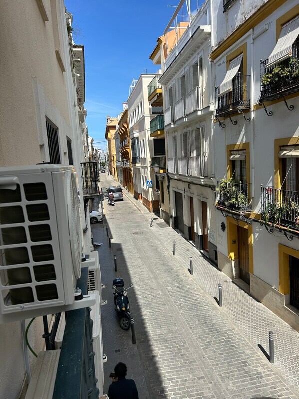 A narrow cobblestone street flanked by buildings with balconies and a clear blue sky.