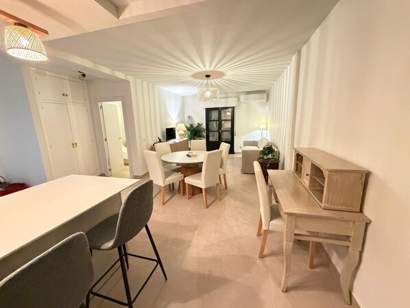 A modern dining area with a round table, chairs, and a bench. There is a white cabinet and a small wooden table.