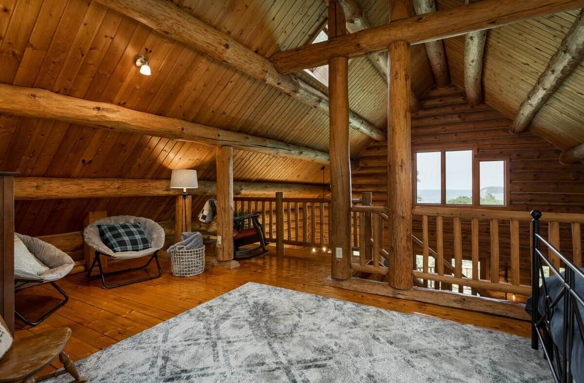 Ein gemütliches Dachzimmer mit Holzbalkendecke, Blick durch ein Fenster und einer Holzwand.