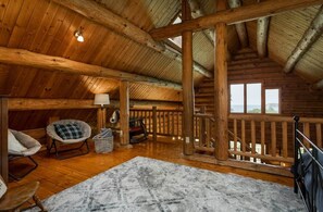 Una habitación acogedora en el ático con techo de madera, vistas a través de una ventana y barandilla de madera.