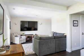 Una sala de estar moderna con un sofá gris, un sillón escocés, un televisor de pantalla plana y una mesa de centro de madera.