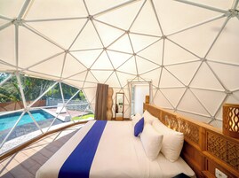 Una habitación con una cama grande, vistas a una piscina exterior y una estructura de techo geométrica.