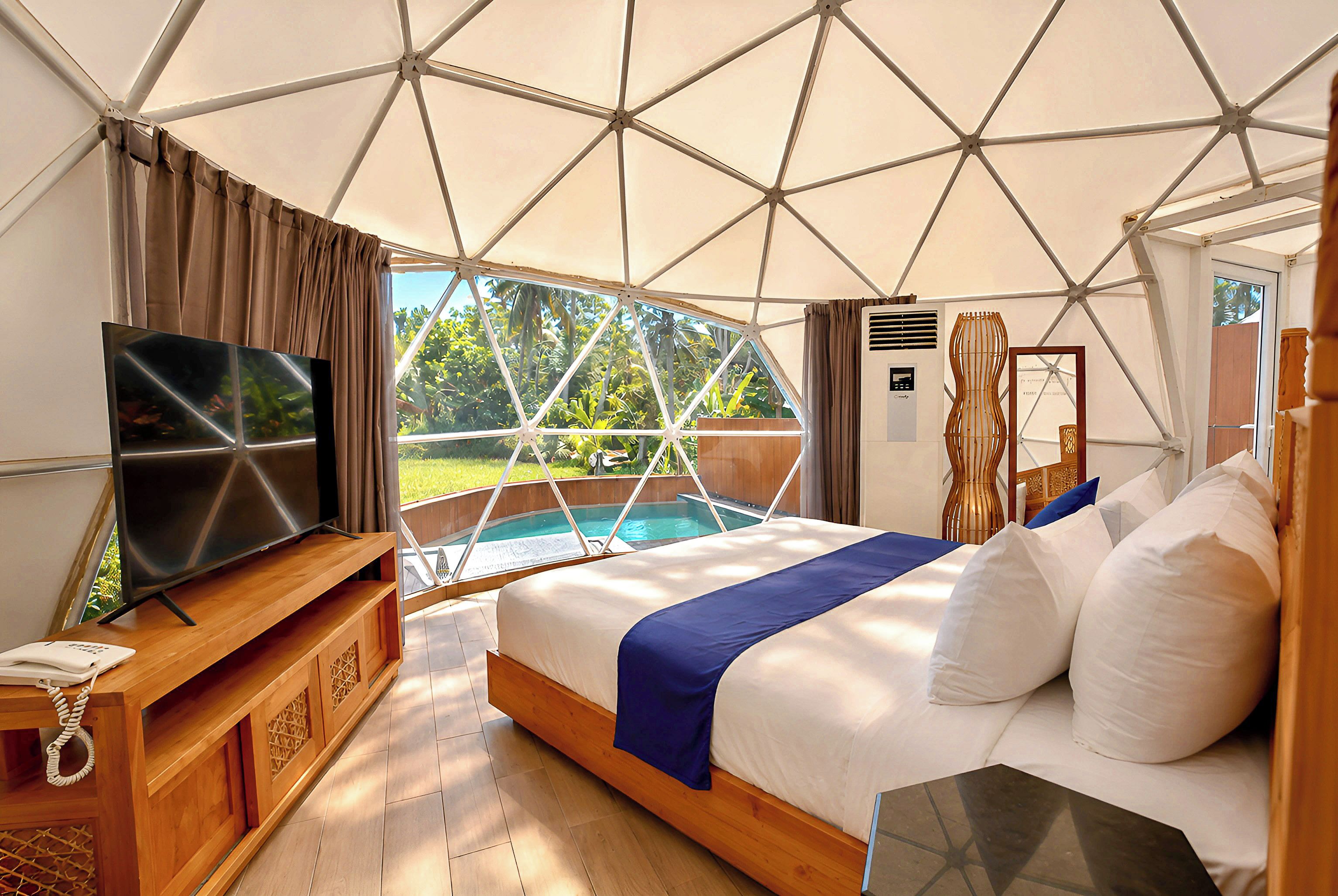 A bedroom with a bed, a TV, a wooden dresser, and a view of a pool and greenery.