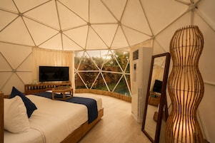 Habitación tipo tienda con cama, televisor y vistas al verdor exterior.