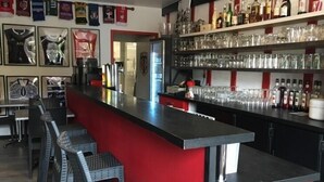 Eine Barbereich mit einer roten Theke, Barhocker und Regalen voller Flaschen und Gläsern.