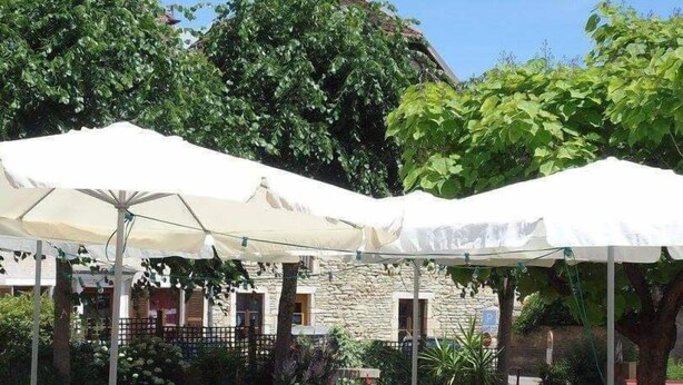 Ein Essbereich im Freien mit Tischen und Stühlen unter weißen Sonnenschirmen, umgeben von Grünpflanzen und einem Steinhaus.