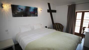 Un dormitorio con cama, una cruz en la pared, una silla y una ventana con cortinas.