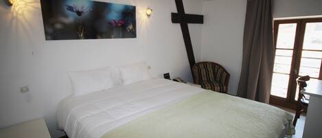 Un dormitorio con cama, una cruz en la pared, una silla y una ventana con cortinas.