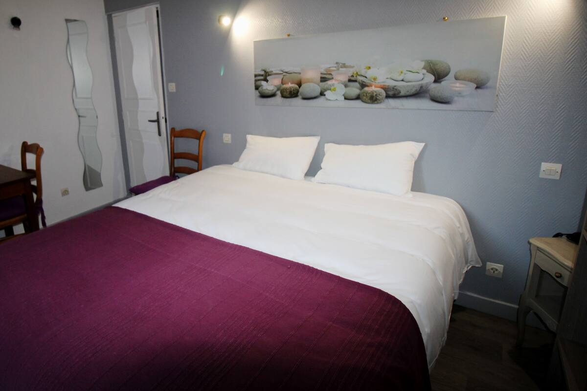 Quarto com cama, cadeira, mesa de cabeceira e uma obra de arte na parede.
