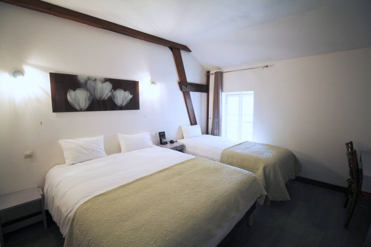 Quarto de hotel com duas camas, um quadro na parede e uma cadeira de madeira.