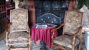 Ein traditionell eingerichtetes Zimmer mit Kamin, zwei verzierten Sesseln, einem Tisch mit Zeitschriften und einer großen Pflanze.