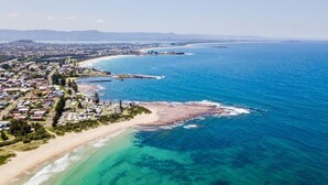 An aerial view of a coastal town with a beach, clear blue waters, and a marina. - Modern Beach Getaway  (Shellharbour)
