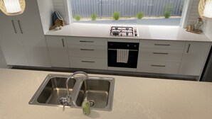 A modern kitchen with a stainless steel sink, a gas stove, and a built-in oven. - Modern Beach Getaway  (Shellharbour)