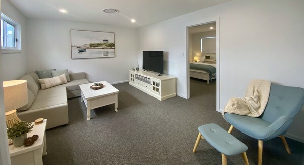 A modern living room with a sofa, a coffee table, a TV, and a blue armchair. - Modern Beach Getaway (Shellharbour)