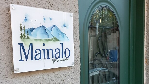 A green door with a glass panel and a sign above it that reads "Mainalo View House." - Mainalo View House - A place for relaxing  (Vytina)