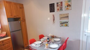 A compact kitchen with wooden cabinets, a refrigerator, and a dining table set with red chairs. - Mainalo View House - A place for relaxing  (Vytina)