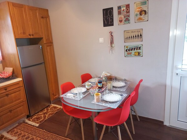 Cocina compacta con refrigerador, gabinetes de madera y mesa de comedor lista para cuatro personas, con sillas rojas.