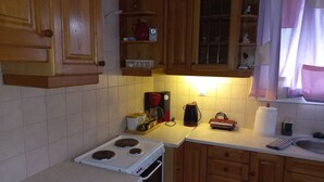 A kitchen with wooden cabinets, a stove, a coffee maker, and a window with curtains. - Mainalo View House - A place for relaxing  (Vytina)