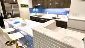 A modern kitchen with dark wooden cabinets, a marble countertop, and a built-in brick accent wall. - Discovery Bay-Resolution Ocean View Condo (Honolulu)