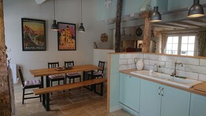 Un coin repas avec une table et des chaises en bois, une cuisine avec des meubles bleu clair et un évier, et deux lampes suspendues.