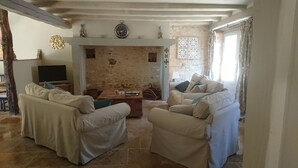 Una sala de estar acogedora con dos sofás beige, una mesa de centro de madera, un televisor sobre un mueble y una chimenea de piedra.