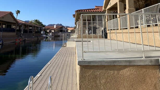Ein Hotel am Wasserufer mit einer Holzsteganlage, die sich ins ruhige Wasser erstreckt, einem überdachten Außenbereich und Blick auf die entfernten Berge.