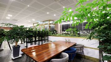 Un espacio interior moderno con una mesa de madera, sillas y plantas en macetas.